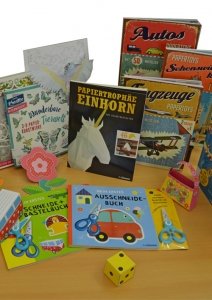 Bastelmaterialien und Bücher für Kinder, darunter das Buch "Papiertröphäe Einhorn", verschiedene Bastelsets und Papierschneider.