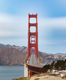 Die Golden Gate Bridge in San Francisco, eine ikonische rot gestrichene Hängebrücke, die sich majestätisch über die Bucht spannt, umgeben von sanften Hügeln und klarem Himmel.