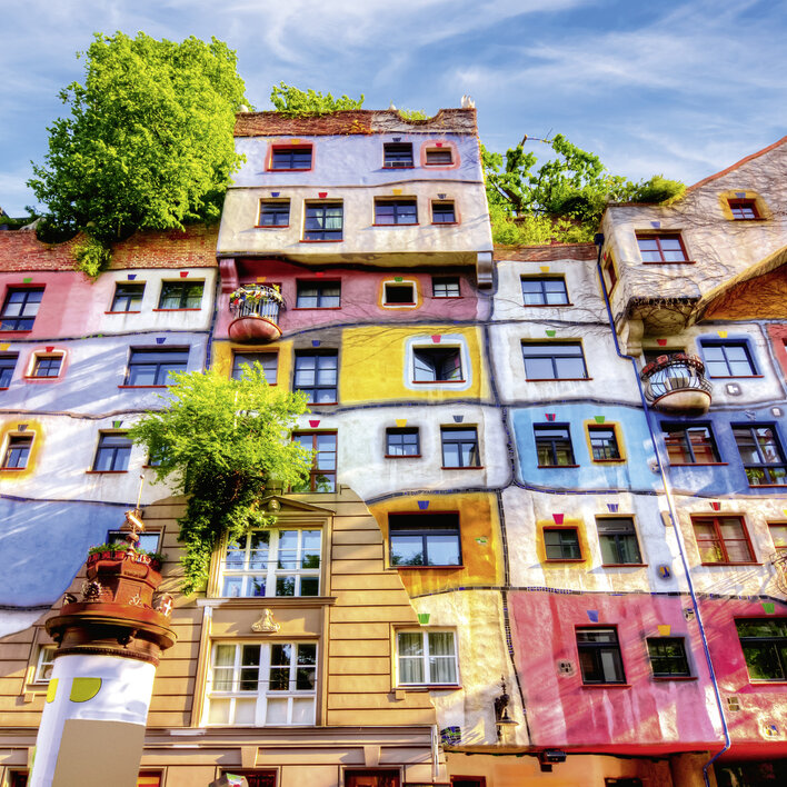 Farbige Wohnhausfassade mit Pflanzen und Balkonen in einer urbanen Umgebung.