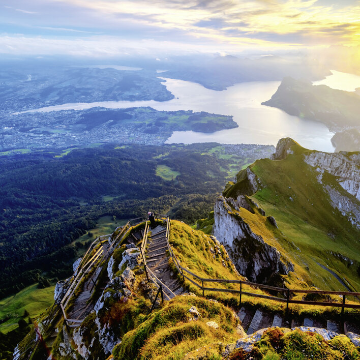 Blick von einem Berggipfel auf einen malerischen See und die umliegende Landschaft bei Sonnenuntergang.